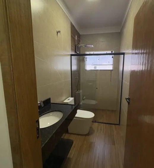 Banheiro com piso amadeirado, revestimento claro e bancada escura.
